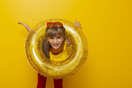 Foto de Niña jugando con un anillo de natación inflable, preparándose para las vacaciones de verano en la playa, aislada sobre fondo de color amarillo - Imagen libre de derechos