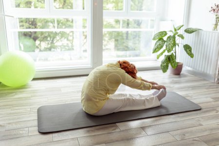 Téléchargez les photos : Femme âgée active faisant de l'entraînement de yoga à la maison concept de mode de vie sain et actif - en image libre de droit