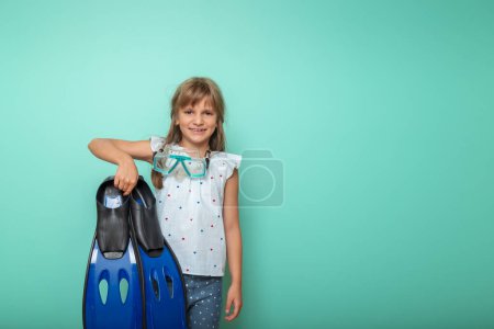 Foto de Niña emocionada preparándose para las vacaciones de verano en la playa, sosteniendo un par de aletas de pie completo y máscara de snorkel, aislado sobre fondo de color menta - Imagen libre de derechos