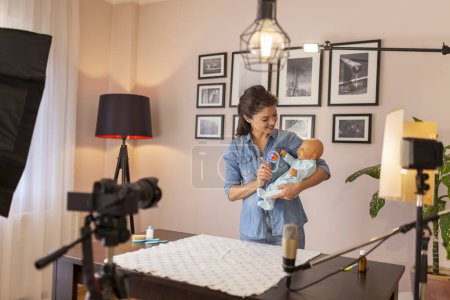 Foto de Tutorial de filmación de vlogger femenina sobre cuidado del bebé recién nacido, manejo y posicionamiento del bebé como parte de clases prenatales en línea - Imagen libre de derechos