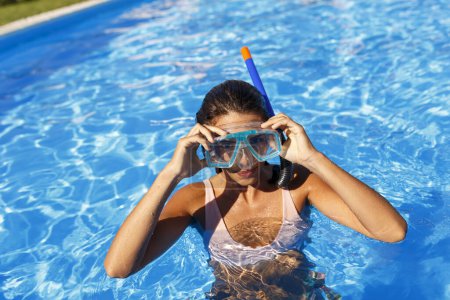 Téléchargez les photos : Belle jeune femme profitant de vacances d'été portant un masque de plongée avec tuba, s'amusant à faire de la plongée avec tuba dans la piscine - en image libre de droit