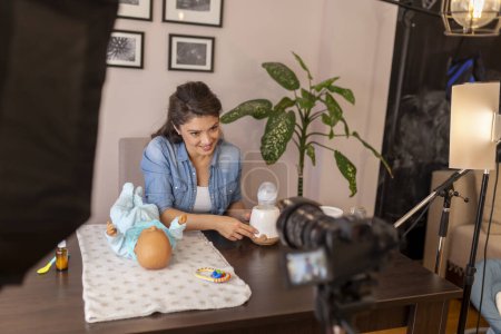 Photo for Female vlogger recording video about baby bottle milk heating in an household appliance as part of online prenatal classes course - Royalty Free Image