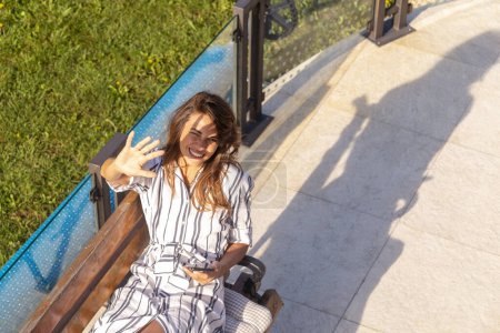 Téléchargez les photos : Vue grand angle d'une belle jeune femme se relaxant dans la cour de sa maison et en utilisant un téléphone intelligent - en image libre de droit