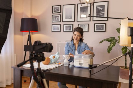 Photo for Healthcare specialist filming video about baby bottles sterilizing with help of electric steam sterilizer as part of online prenatal classes course - Royalty Free Image