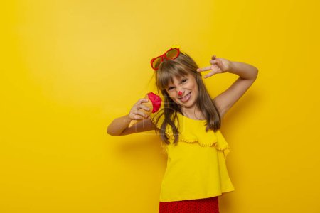 Foto de Hermosa niña divirtiéndose mientras come helado en un cono aislado sobre fondo de color amarillo - Imagen libre de derechos