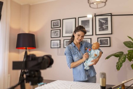 Photo for Female vlogger filming tutorial about newborn baby care, baby handling and positioning as part of online prenatal classes - Royalty Free Image