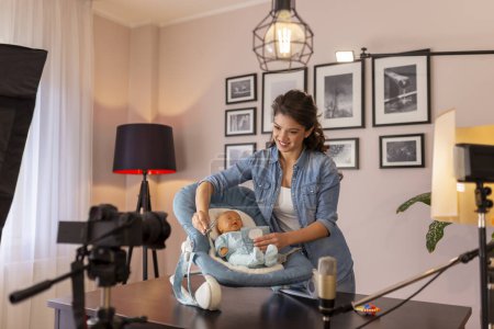 Photo for Female vlogger making video about the use of newborn baby rocker for putting baby to sleep easier as part of online prenatal classes course - Royalty Free Image