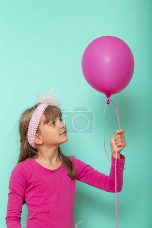 Foto de Retrato de una hermosa niña celebrando su cumpleaños, sosteniendo un globo rosa, aislado sobre fondo de color menta - Imagen libre de derechos