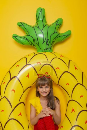 Photo for Child sitting in an inflatable pineapple shaped swim ring, getting ready for beach summer vacation, isolated on yellow colored background - Royalty Free Image