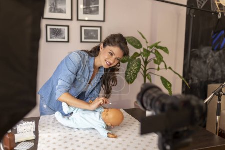 Photo for Healthcare specialist recording video about cleaning newborn baby ears with safety cotton ear buds as part of online birthing classes course - Royalty Free Image