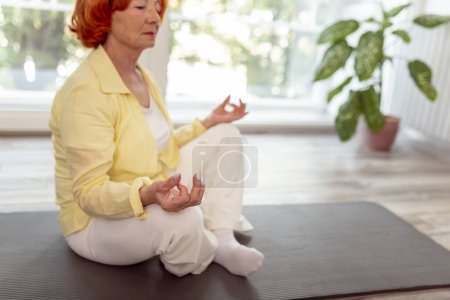 Téléchargez les photos : Femme âgée active pratiquant la méditation à la maison concept de mode de vie sain - en image libre de droit