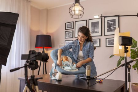 Photo for Female vlogger recording video about the use of newborn baby rocking chair for getting baby to sleep easier as part of online prenatal classes course - Royalty Free Image