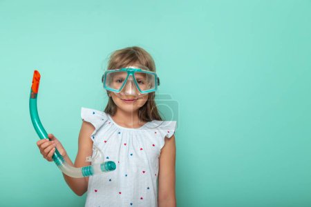 Téléchargez les photos : Petite fille excitée se préparant pour les vacances d'été à la plage, tenant masque de plongée, isolé sur fond de couleur menthe - en image libre de droit