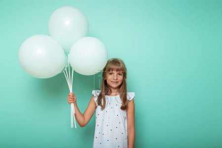 Foto de Retrato de una hermosa niña sosteniendo un ramo de globos y sonriendo, aislado sobre fondo de color menta con espacio para copiar - Imagen libre de derechos