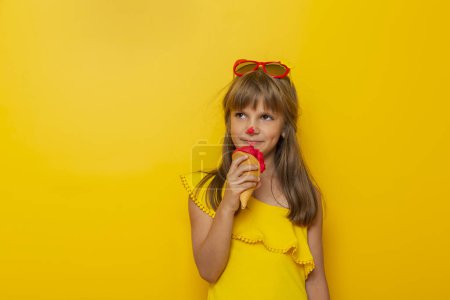 Foto de Niña divirtiéndose mientras come helado en un cono aislado sobre fondo de color amarillo - Imagen libre de derechos