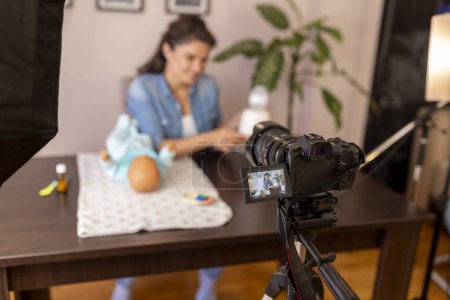 Photo for Female vlogger recording video about baby bottle milk preparation and heating in an household appliance as part of online prenatal classes course - Royalty Free Image