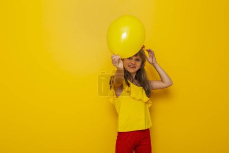 Photo for Child having fun while playing with a yellow balloon isolated on yellow colored background - Royalty Free Image