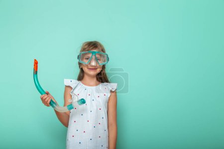 Téléchargez les photos : Petite fille excitée se préparant pour les vacances d'été à la plage, portant un masque de plongée, isolé sur fond de couleur menthe - en image libre de droit