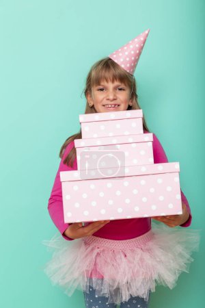 Photo for Beautiful little girl wearing party hat, celebrating her birthday and holding a bunch of birthday presents, isolated on mint colored background - Royalty Free Image