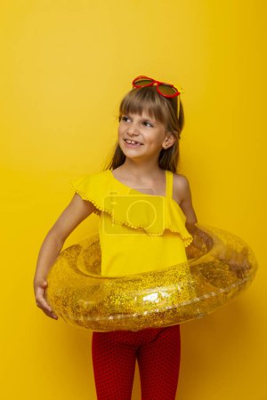 Foto de Niña sosteniendo un anillo de natación inflable, preparándose para las vacaciones de verano en la playa, aislada sobre fondo de color amarillo - Imagen libre de derechos