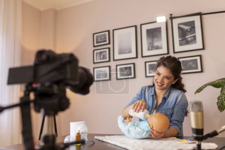 Photo for Female vlogger recording video about newborn baby bottle feeding and baby handling as part of online prenatal classes course - Royalty Free Image
