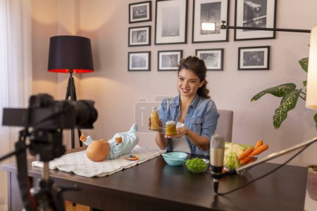 Photo for Female vlogger filming video about introducing soft food to baby nutrition and preparation of fresh fruit and vegetable porridges as part of online prenatal classes course - Royalty Free Image
