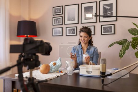 Photo for Healthcare specialist filming video about baby bottles sterilizing with help of electric steam sterilizer as part of online birthing classes course - Royalty Free Image
