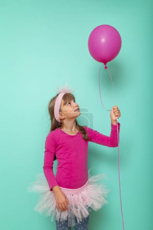 Foto de Hermosa niña usando una falda de ballet, sosteniendo un globo rosa, aislado sobre fondo de color menta - Imagen libre de derechos