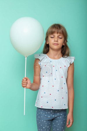 Foto de Retrato de una hermosa niña sosteniendo un globo con los ojos cerrados, aislado sobre fondo de color menta - Imagen libre de derechos