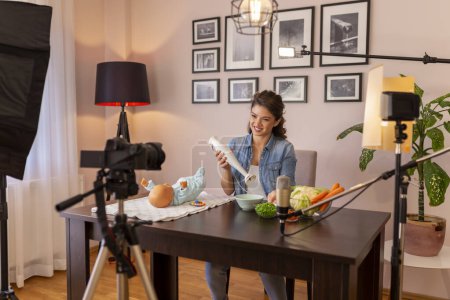 Photo for Vlogger filming video about introducing soft food to baby nutrition and preparation of fresh fruit and vegetable porridges using stick mixer as part of online birthing classes course - Royalty Free Image