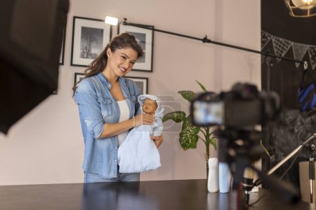 Photo for Midwife recording video about handling newborn baby after bathing, wrapping it in towel, holding and drying; influencer making tutorial of newborn baby handling - Royalty Free Image