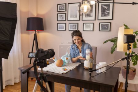 Photo for Female vlogger filming video about baby bottle milk preparation and heating in an household appliance as part of online prenatal classes course - Royalty Free Image