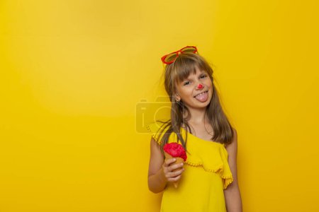 Photo for Little girl having fun while eating ice cream in a cone isolated on yellow colored background - Royalty Free Image