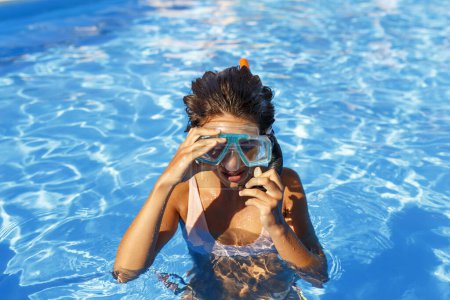 Foto de Hermosa joven disfrutando mientras está en vacaciones de verano poniéndose una máscara de snorkel, divirtiéndose haciendo snorkel en la piscina - Imagen libre de derechos