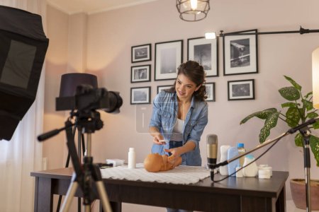 Photo for Influencer recording video about newborn baby care products and the use of baby powder to prevent diaper rash as part of online birthing classes course - Royalty Free Image