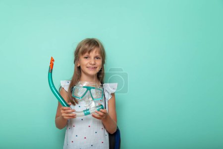 Photo for Excited little girl getting ready for beach summer vacation, holding snorkeling mask, isolated on mint colored background - Royalty Free Image