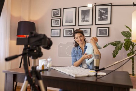 Photo for Influencer recording video about newborn baby burping positions and baby handling after feeding as part of online prenatal classes - Royalty Free Image