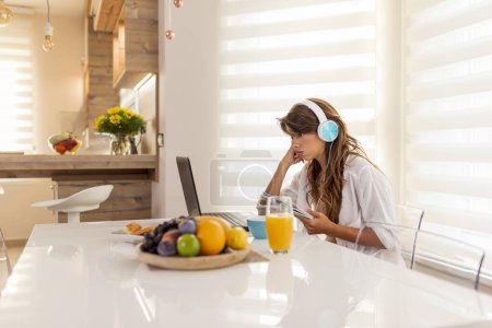 Photo for Woman taking an online class course, wearing headset and writing in a planner while listening to a lesson - Royalty Free Image