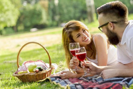 Photo for Couple in love lying on a picnic blanket, holding glasses of wine and making a toast - Royalty Free Image
