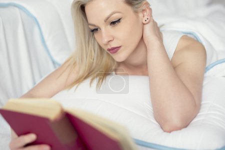 Foto de Hermosa joven acostada en la cama, leyendo un libro - Imagen libre de derechos