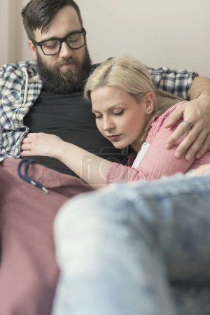 Téléchargez les photos : Jeune couple se reposant après une journée bien remplie au travail, couché sur un canapé et étreignant - en image libre de droit