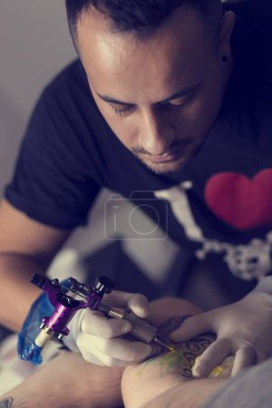 Foto de Artista de tatuajes masculino sosteniendo una pistola de tatuaje, mostrando un proceso de hacer tatuajes en el brazo de un modelo tatuado masculino. - Imagen libre de derechos