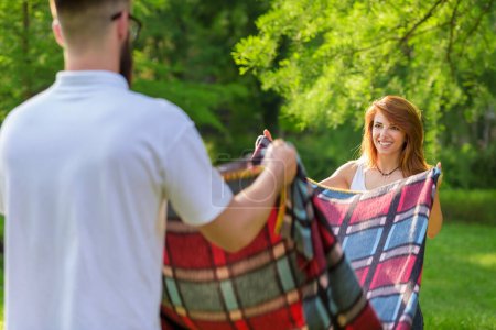 Téléchargez les photos : Couple amoureux plaçant une couverture de pique-nique sur une prairie. Loisirs et détente dans la nature - en image libre de droit