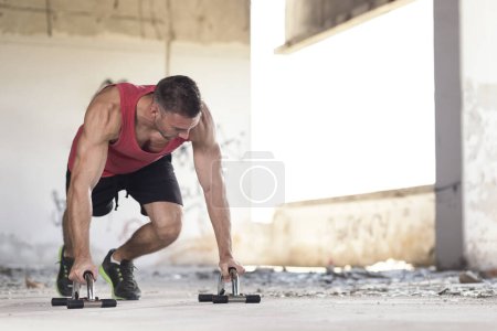 Téléchargez les photos : Musclé, athlétique, jeune homme faisant des pompes dans un bâtiment en ruine abandonné - en image libre de droit