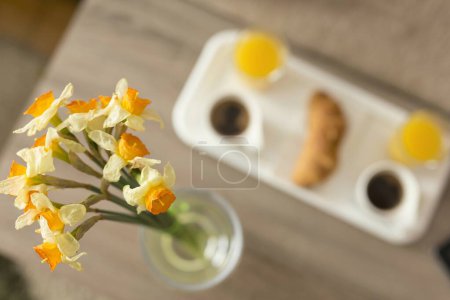 Téléchargez les photos : Vue du dessus d'un plateau de petit déjeuner sur une table dans une chambre d'hôtel, mise au point sélective sur l'une des fleurs dans un vase à côté d'un plateau - en image libre de droit