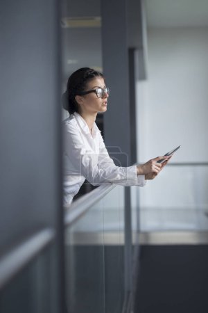 Téléchargez les photos : Femme d'affaires forte, confiante et debout dans un couloir d'immeuble de bureaux, tenant un ordinateur tablette - en image libre de droit