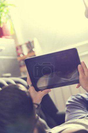 Foto de Modelo masculino acostado en un sofá en una sala de estar, navegando por la web en una tableta - Imagen libre de derechos