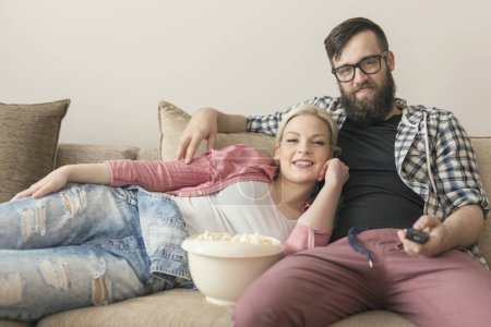 Téléchargez les photos : Couple amoureux assis sur le canapé dans le salon, regarder la télévision et manger du pop-corn. Concentre-toi sur la fille - en image libre de droit