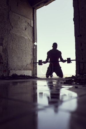Foto de Musculoso, atlético, joven atleta levantando pesas en un edificio en ruinas junto a un charco de agua - Imagen libre de derechos