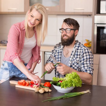 Foto de Hermosa pareja joven rebanando verduras para ensalada en una cocina moderna - Imagen libre de derechos